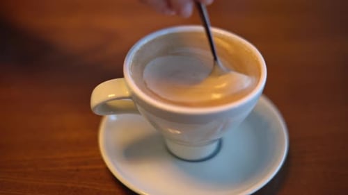 Stirring Creamy Coffee in White Cup Close Up