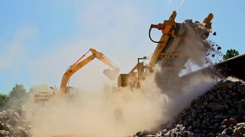 Slow Motion shot of crane and conveyor transporting rocks and sand with dust in sunlight - low angle
