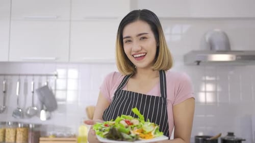 Smiling Woman Presents a Healthy Salad in Kitchen