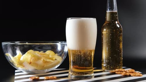 Kaltes Bier mit Snacks vor dunklem Hintergrund einschenken