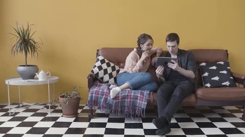 Young Couple Relaxing on Sofa Browsing Tablet Together in Cozy Living Room