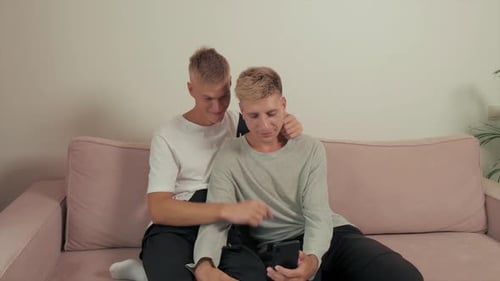 LGBT Couple Gay Couple Together at Home on the Couch Lie Hold a Phone in Hand