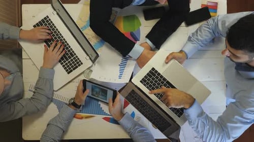 Top View to Hands of Employees Using Laptops and Graphs for Planning Future Project Indoor