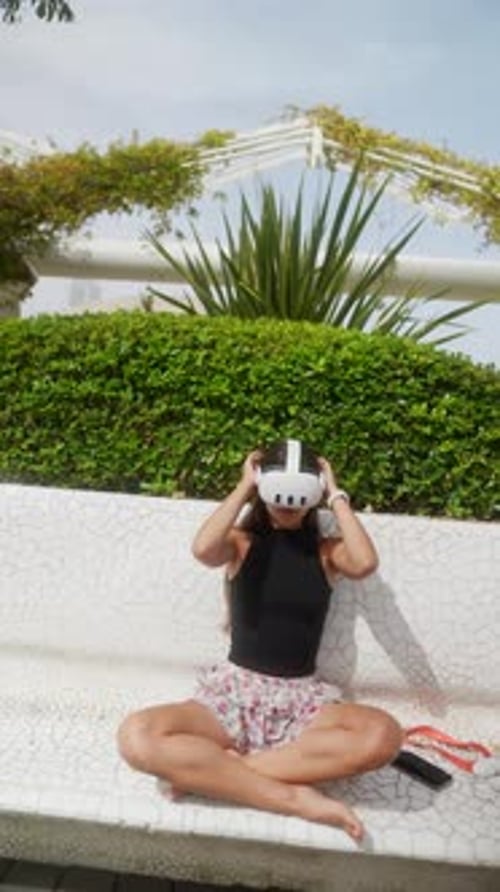 In an Urban Park a Lady Relaxes on a Bench in VR Glasses Enjoying the Outdoor Experience