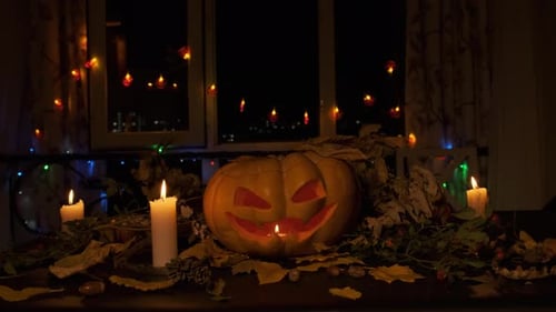 Holiday background with carved glowing pumpkin surrounded by shining candles