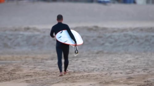 Man walks on the beach ready to start his surfing trip in the water