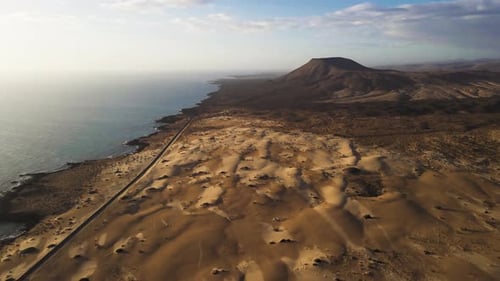 Aerial view of sand dunes and ocean with coastal road, Spain.