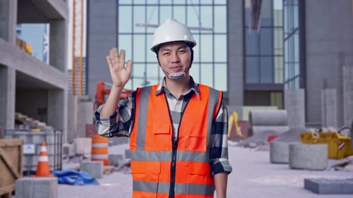 Asian Male Engineer Smiling To Camera And Waving Hand Saying Bye at Construction Site