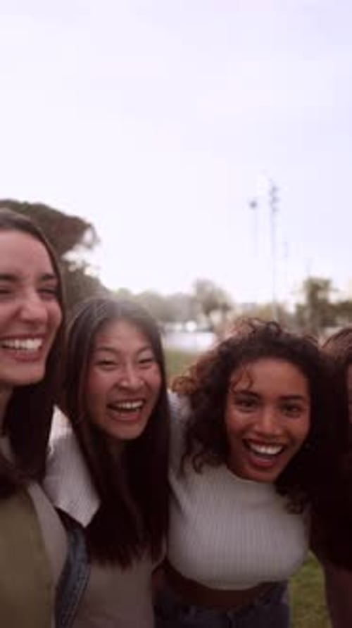 Four cheerful female friends are enjoying a sunny day at the park, laughing and embracing each other