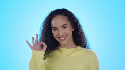 Okay sign, happy and face of woman in studio for approve, agreement or perfect on blue background
