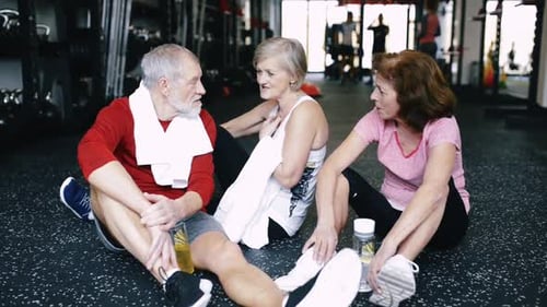 Fit Seniors in Gym Sitting on the Floor, Resting, Discussing Fitness Progress 60s