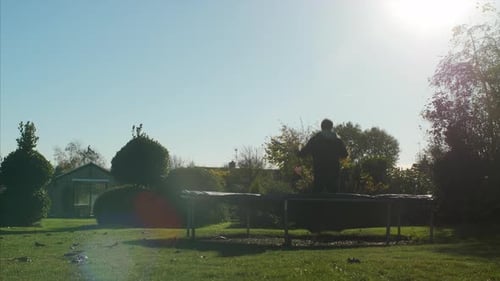 A man kicking his legs to the side whilst jumping on a trampoline. WIDE STATIC SHOT with LENS FLARE.