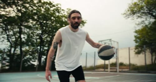 Un homme en t-shirt blanc et short noir dribble habilement un ballon de basket sur un terrain de basket