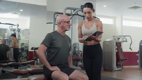Female Coach Using Tablet when Explaining Training Plan to Man in Gym