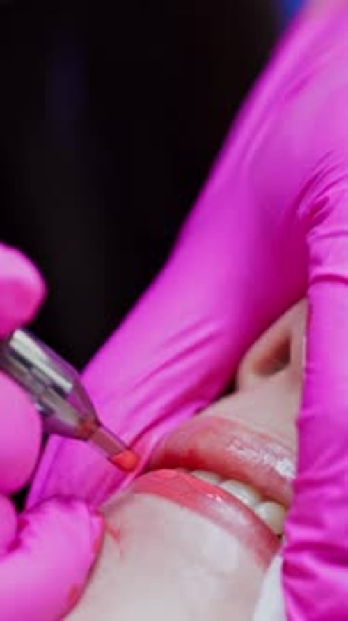 Lips tattoo. Cosmetologist in pink gloves applying permanent makeup tattoo on lips.