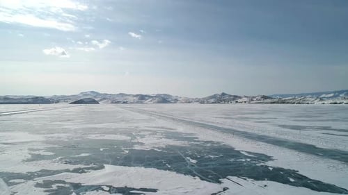 Aerial Over Snow Covered Cracked Ice of Frozen Baikal and Snowcapped Mountains Ice Road Beautiful