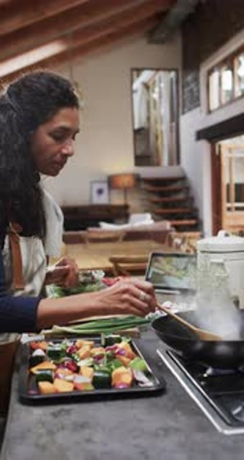 Vertical video of biracial woman in apron preparing meal in kitchen, slow motion