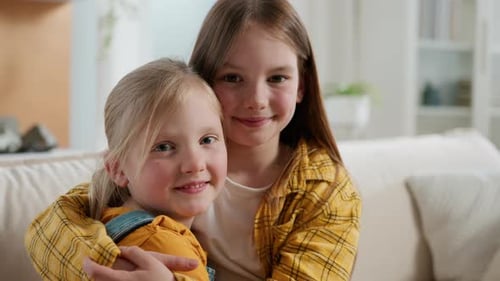 Two Smiling Girls Embrace Affectionately Indoors During Daytime