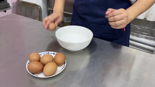 Pastry dessert making in progress, patissier cracking eggs into bowl commercial restaurant setting.
