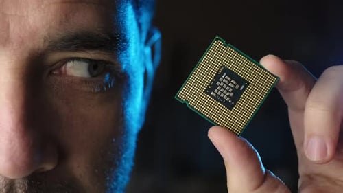 Meia-face masculina olhando para o processador de microchip da CPU na mão, fundo preto. De perto