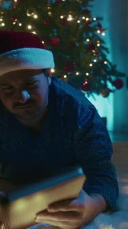 Young Man In Pajamas Lying On The Floor Having Fun Magic Book On Christmas Night