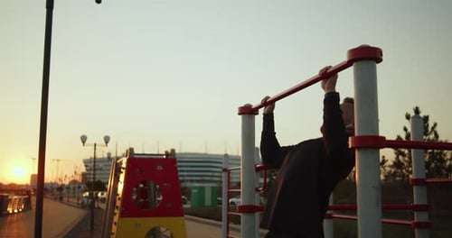 Young Athletic Man Works Out Doing Pullups on a Street Sports Ground at Sunset