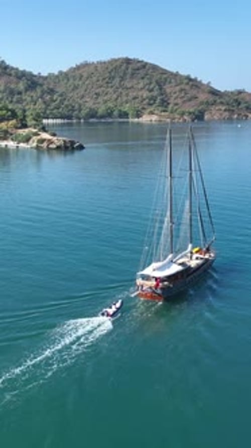 Aerial view: Yacht sails with jetski in calm water