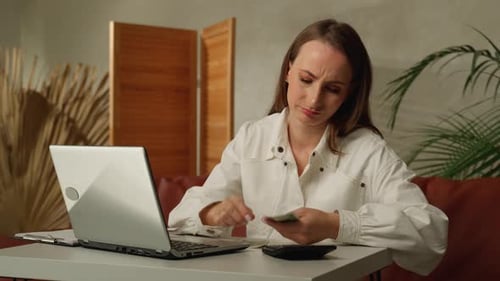 A Frustrated Young Woman Working on Finances at Home Counting Money Dressed in a White Shirt Sitting