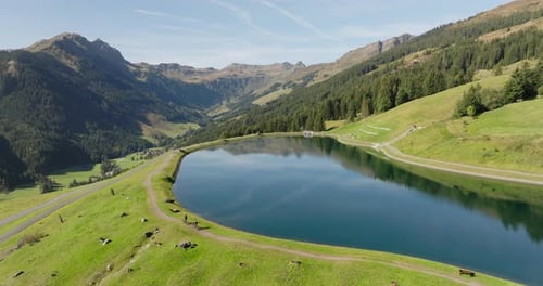 People Cycling On Biking Trail By Lake With Mountain Views