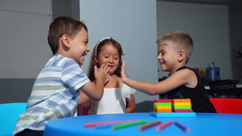 Children Play Hand Clapping Game at Table Indoors