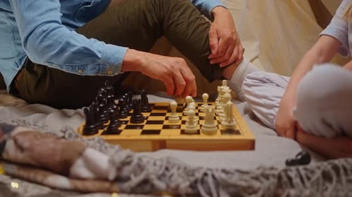 Nahaufnahme Die Hand des Vaters bewegt Schachfiguren auf dem Schachbrett und bringt ihrer kleinen Tochter das Schachspielen bei
