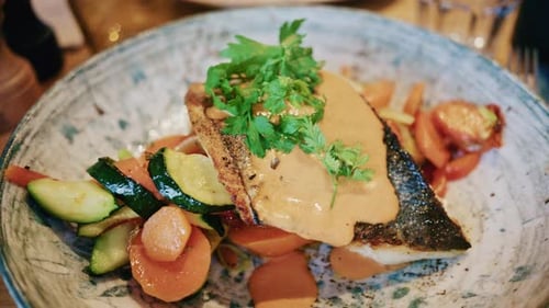 Close up of a plated fish fillet served with vegetables and creamy sauce in a restaurant setting
