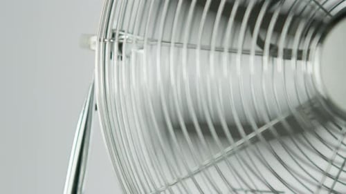 Schwarze Lüfterblätter eines metallischen Lüfters in Zeitlupe vor weißem Hintergrund