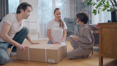 A boy and his parents are unpacking a package together in a large cardboard box.