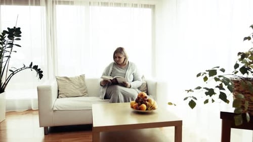 Woman Reading Book Sitting on Couch Indoors