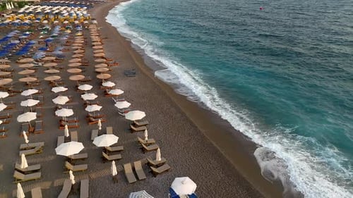 Mediterranean beach with colorful umbrellas and calm waves breaking on shore at sunrise