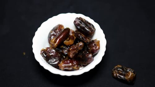 fresh dates dropping in ceramic bowl with black background studio shot