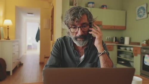Reifer Geschäftsmann arbeitet am Laptop und spricht am Handy