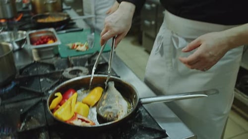 Head Chef Frying Fish with Bell Peppers at Work in Restaurant Kitchen
