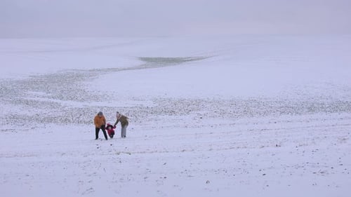 A Family of Three Walks Playfully Towards the Camera on a Snowy Hill