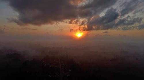 A Sunrise Over A Village Shrouded In Mist And Dramatic Cloudscape