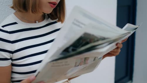 Woman Reads Newspaper Sitting Near White Building
