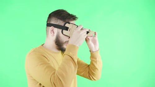 Excited young man puts on virtual reality headset in greenbox studio for immersive gaming