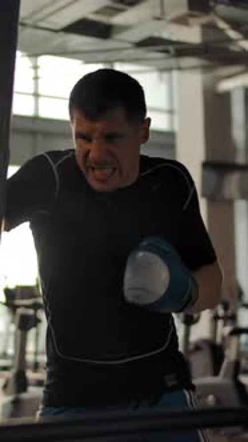 Vertical of Aggressive Athlete Boxer Hits a Punching Bag in the Gym