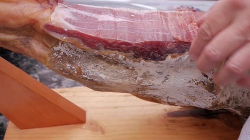 Side view of spanish jamon leg, ham leg, on holder for cutting. Large knife slicing thin cuts. Pork