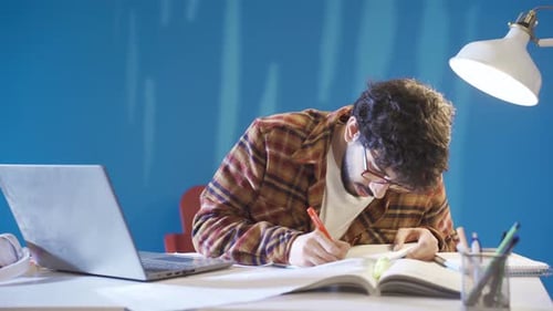 Young Adult Studying at Desk with Laptop and Book