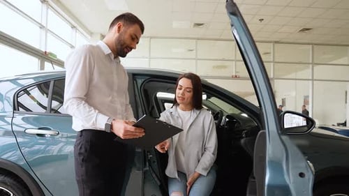 Salesperson in Car Showroom Showing a Car to Female Customer Right Hand Drive Car