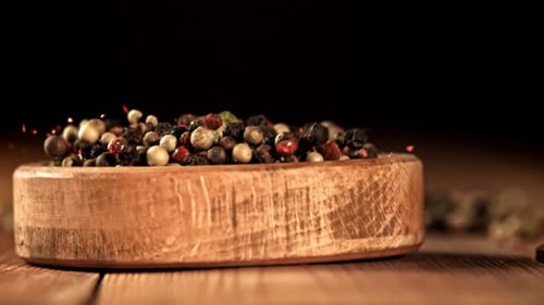 Colorful Peppercorns Falling into Wooden Bowl on Table
