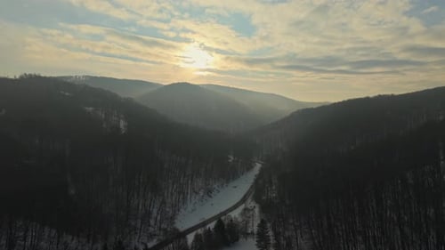 A panoramic view of snow-covered mountains and a dense forest during winter. A winding road cuts
