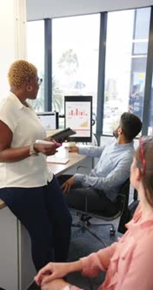 Vertical video: Presenting data on tablet, business team discussing charts in modern office